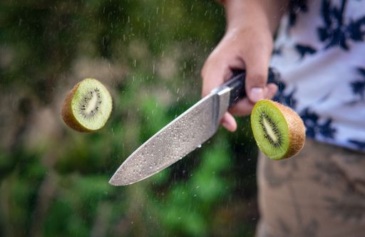 A closeup shot of a male with a knife in hand cutting kiwi in half