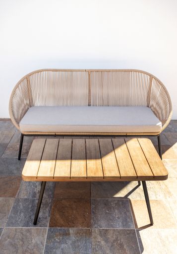 A vertical shot of the empty garden sofa with a wooden table outdoors.