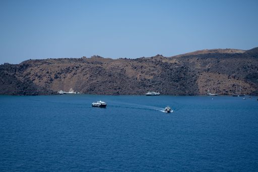 The boats floating on the crystal-clear blue water of a tranquil beach surrounded by lush green hills