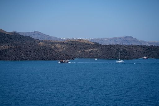 The boats floating on the crystal-clear blue water of a tranquil beach surrounded by lush green hills