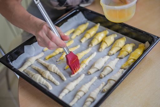 A selective focus shot of a female's hand smearing pastry with egg yolk with a brush