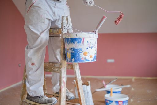 A shallow focus shot of a male standing on a ladder and painting walls with a roller