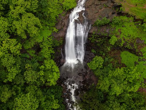 A top drone view of Vihigaon Ashoka WaterFalls flowing through the rocks surrounded by lush greenery