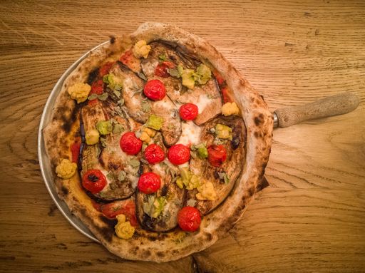 An overhead shot of a vegetarian pizza with cherry tomatoes in a plate on a brown table