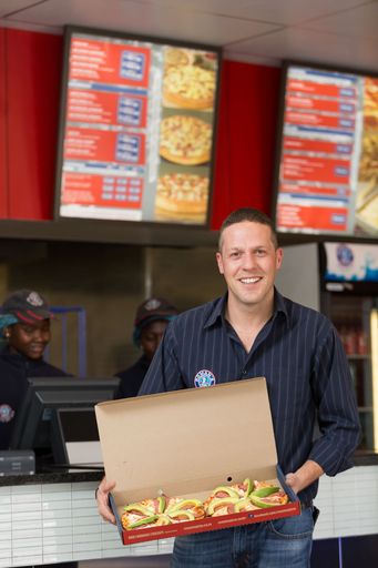 Johannesburg, South Africa - August 11, 2016: Take-out retail store owner holding a pizza at the counter