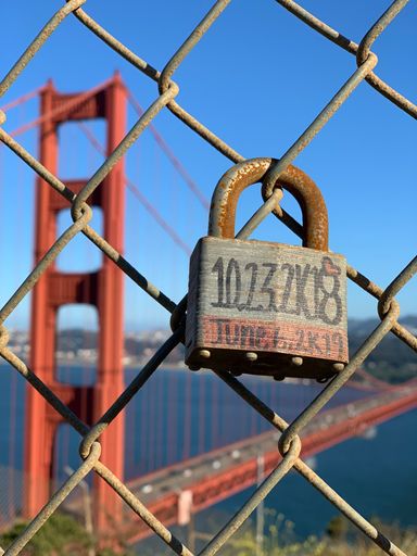 The soft focus of a old padlock hanging from wire mesh fence in front of Golden Gate bridge in San Francisco, California