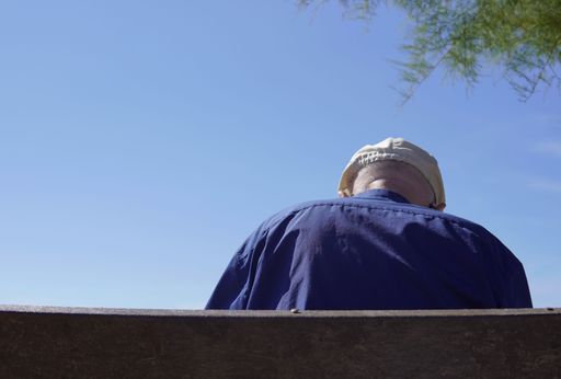 A back view of an elderly gentleman sitting on a bench