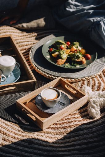 A vertical shot of wooden boards with cappuccinos and a plate of vegetable toast outdoors