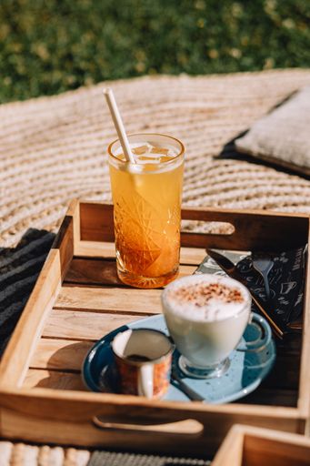 A vertical shot of a wooden breakfast board with a cappuccino and a glass of lemonade