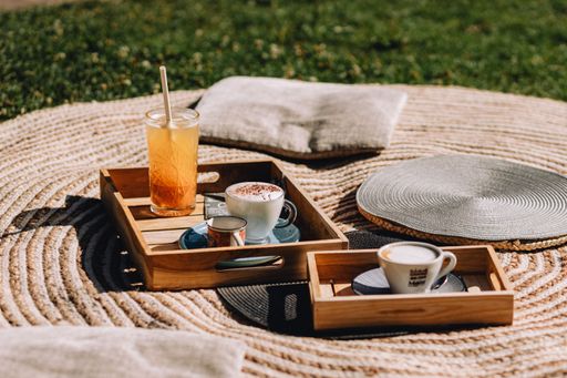 A closeup shot of wooden breakfast boards with a cappuccino and a glass of lemonade