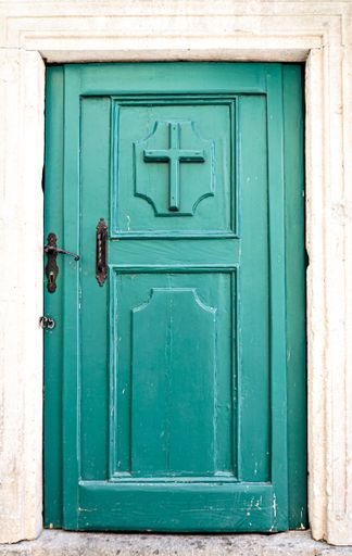 A vertical shot of a green old wooden door with a cross