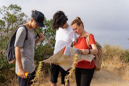 Group of friends with backpacks looking at a map on nature. Freedom, travel and wellness concepts, copy space