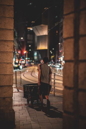 A vertical shot of a young delivery man working at late night and pushing a cart in Wan Chai