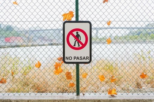 A closeup shot of a prohibition sign in front of a chain-link with autumn leaves, translation: "do not pass"