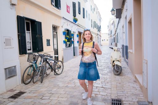an adult woman walks smiling down a cobblestone street in a mideterranean village, tourist visiting Ciudadela, Menorca, Balearic Islands, Spain