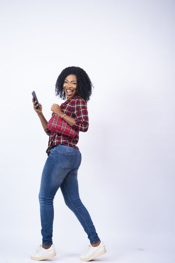 A vertical shot of an excited young African woman walking sideways while using her phone