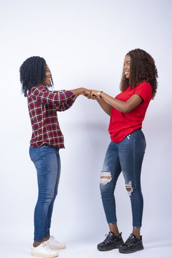 A vertical shot of two beautiful young African women fist-bumping each other, in front of a white background