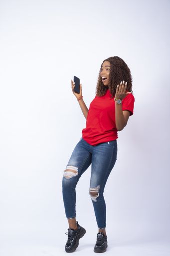 A vertical shot of an excited young African woman holding her phone looking happily towards her side