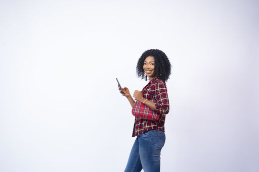 A happy young African woman standing sideways and using her phone
