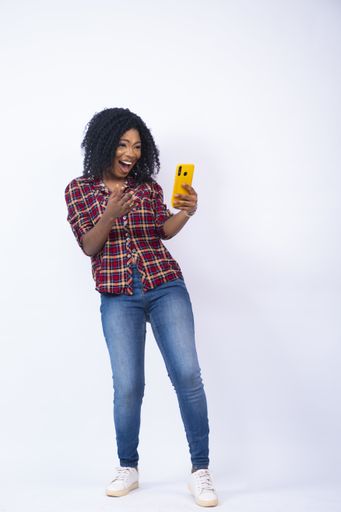 A vertical shot of an excited young black woman feeling surprised and happy while using her phone