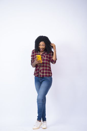A vertical shot of a young black female feeling surprised looking at her phone
