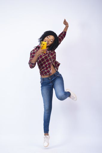 A vertical shot of a happy young African woman holding her phone and jumping in excitement