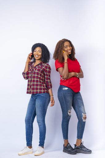 A vertical shot of beautiful young African women making phone calls and standing back to back in front of a white background