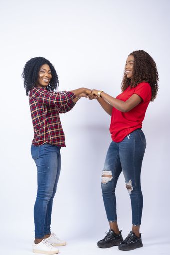 A vertical shot of two beautiful young African women fist bumping while standing in front of a white background