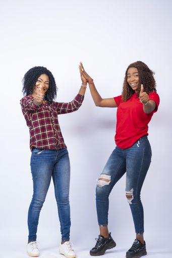 A vertical shot of pretty African females giving high five and a thumbs up