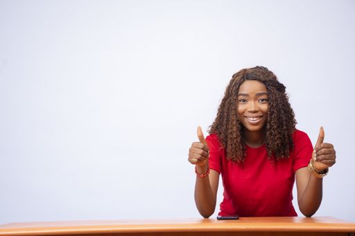 A shot of a black female sitting at a desk giving a thumbs up - advertising concept