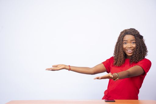 A pretty black woman gestures to the empty space at her side, in front of a white background -advertising concept