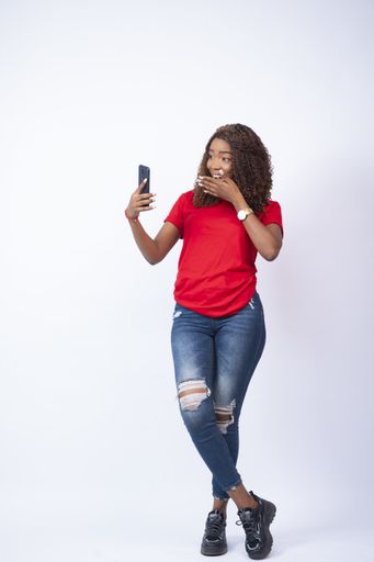 A vertical shot of a beautiful black lady feeling surprised while looking at her phone