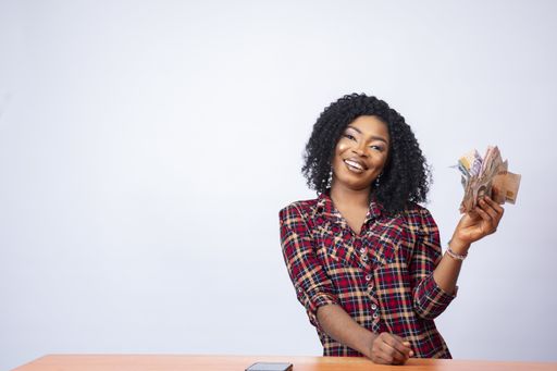 A confident and beautiful young black woman sitting and holding money, in front of a white background
