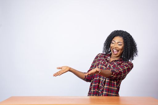 An excited and beautiful African woman sitting at a desk and gesturing to the empty space on her side