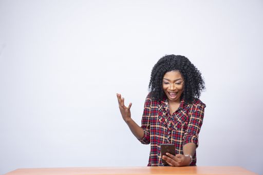 A pretty young black woman looking surprised and excited while looking at her phone