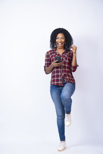A vertical shot of a pretty black female feeling excited while using her phone