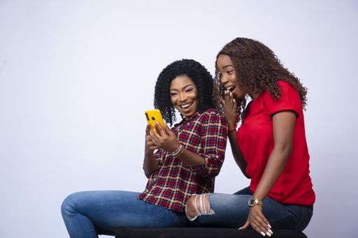 A shot of two beautiful black females sitting together looking surprised and feeling excited while looking at a phone
