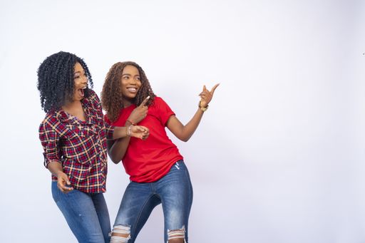 A closeup of two beautiful young black women feeling excited and pointing to the empty space on their side -advertising concept