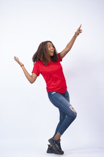 A pretty young African female wearing a red top and blue jeans feeling excited and happy
