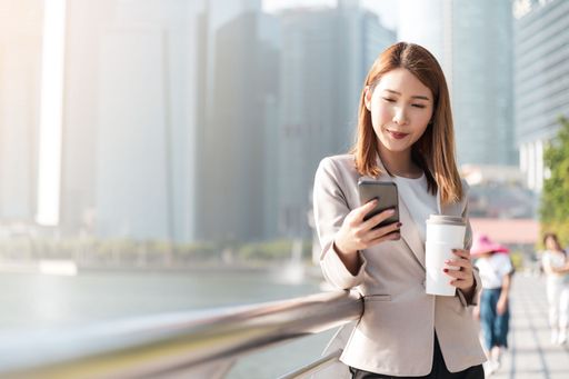 An East Asian Businesswoman talking on the phone and holding a plastic cup with urban background