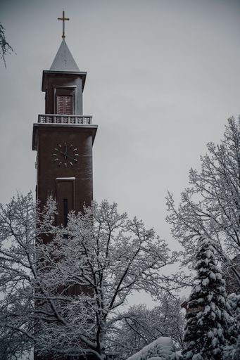 A vertical shot of a church tower with a clock in winter