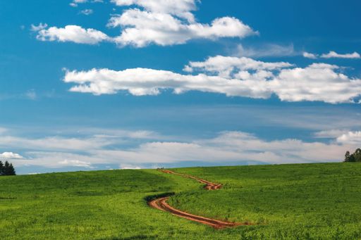 Landscape with a road winding up the green field on the  hill and leading to the cloudy sky