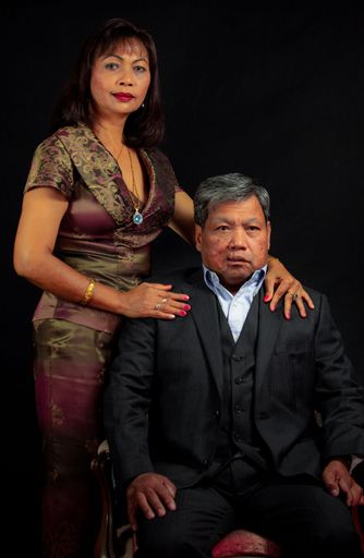 A studio portrait of a middle aged Southeast Asian couple in formal clothes against dark background