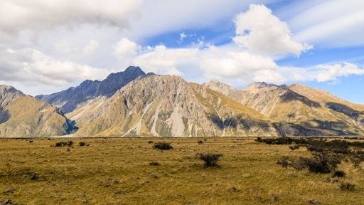 A scenic view of a green field against mountains on a cloudy day in Glentanner, New Zealand