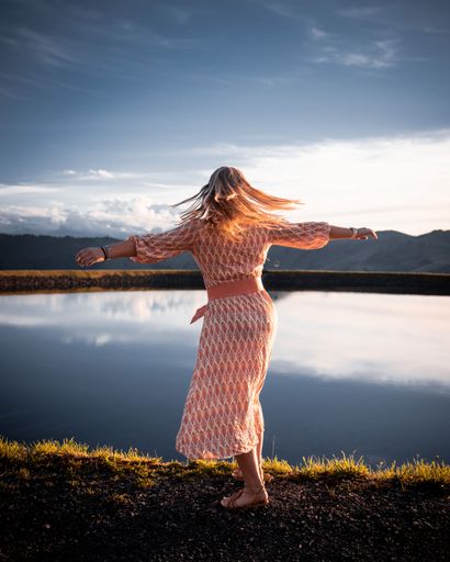 A vertical shot of a young blonde girl with open hands on the lake shore