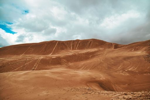 Brown sandy hill dunes under cloudy blue sky