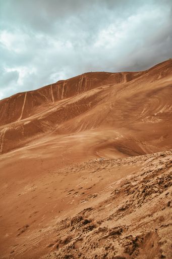 Orange sandy hill dunes under cloudy blue sky, vertical shot