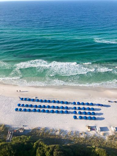 An aerial shot over sandy coast and beach umbrellas by tranquil seawater in the summer