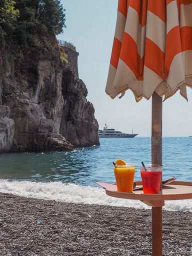 A beach umbrella table with two juicy cocktails on the beach in Positano on the Amalfi coast