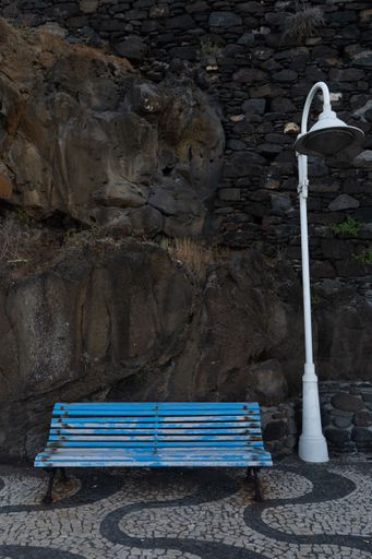 A vertical shot of a blue bench and a lamp near a cliff